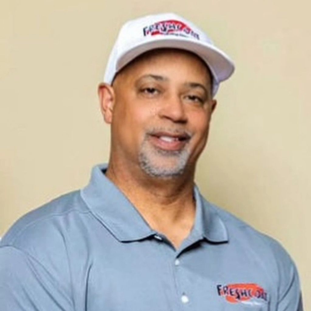Smiling man in a light blue shirt and white cap with a logo.