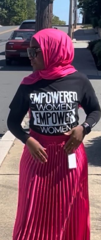 Woman in pink hijab and skirt with an empowering message shirt.