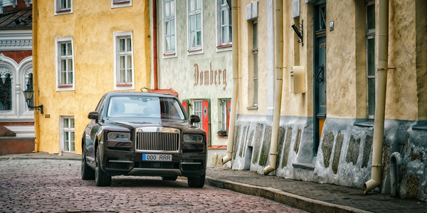 Luxury black Rolls-Royce parked on a cobblestone street beside colorful old buildings.