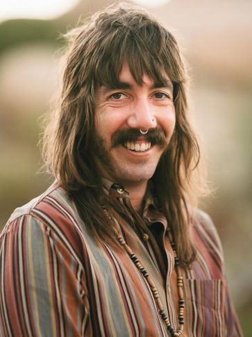 Smiling man with nose rings and a striped shirt.