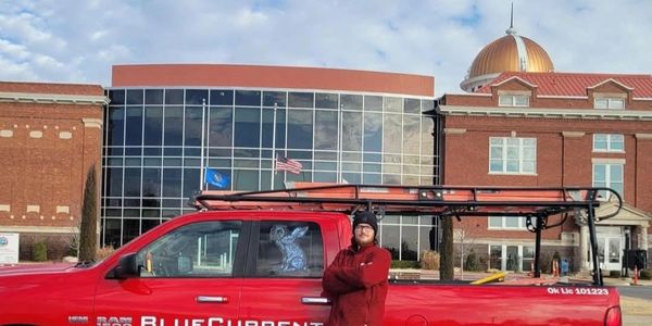 Man stands confidently by a red BlueCurrent Electric truck in front of a large building with a golden dome.