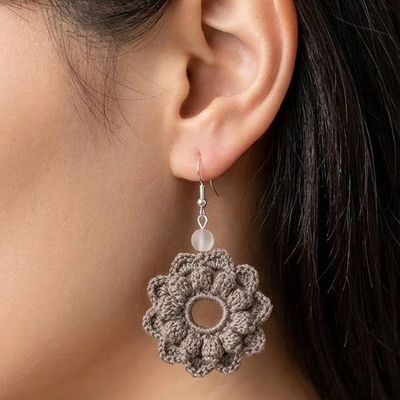Close-up of a crocheted flower earring worn on the ear.