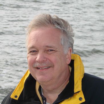 Smiling man with a yellow jacket by the water.