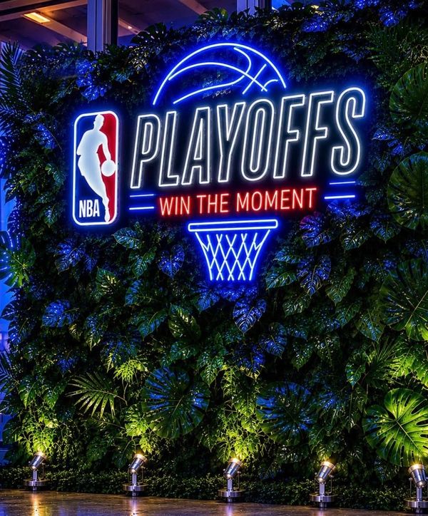 Neon NBA Playoffs sign with slogan on a leafy wall.