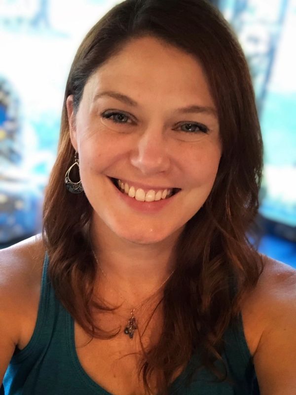 Smiling woman with brown hair wearing a teal top and earrings.