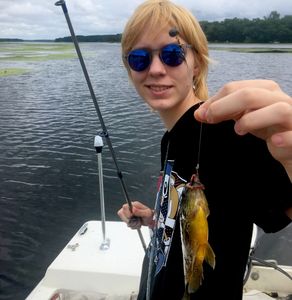 A person wearing a black t-shirt and holding a fish and a fishing road 