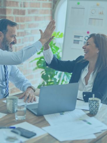 Two colleagues happily high-five in a modern office setting.