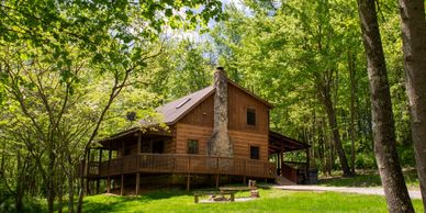Rustic wooden cabin surrounded by lush green trees and grass.