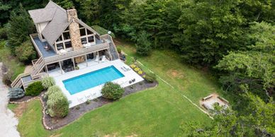 A cozy cabin with a pool nestled in lush greenery and surrounded by trees.