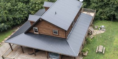 A wooden cabin with a metal roof surrounded by lush green trees.