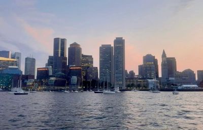 Skyline of a city with tall buildings at sunset over water.