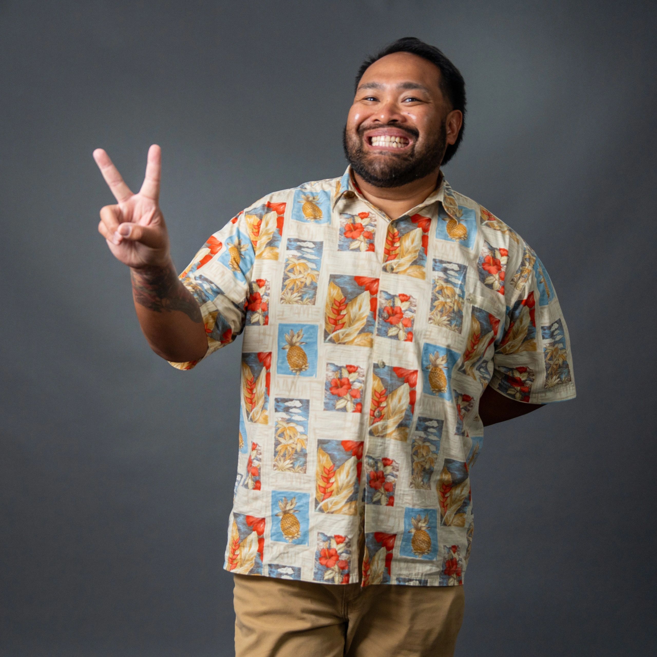 Smiling man in a colorful Hawaiian shirt showing a peace sign.