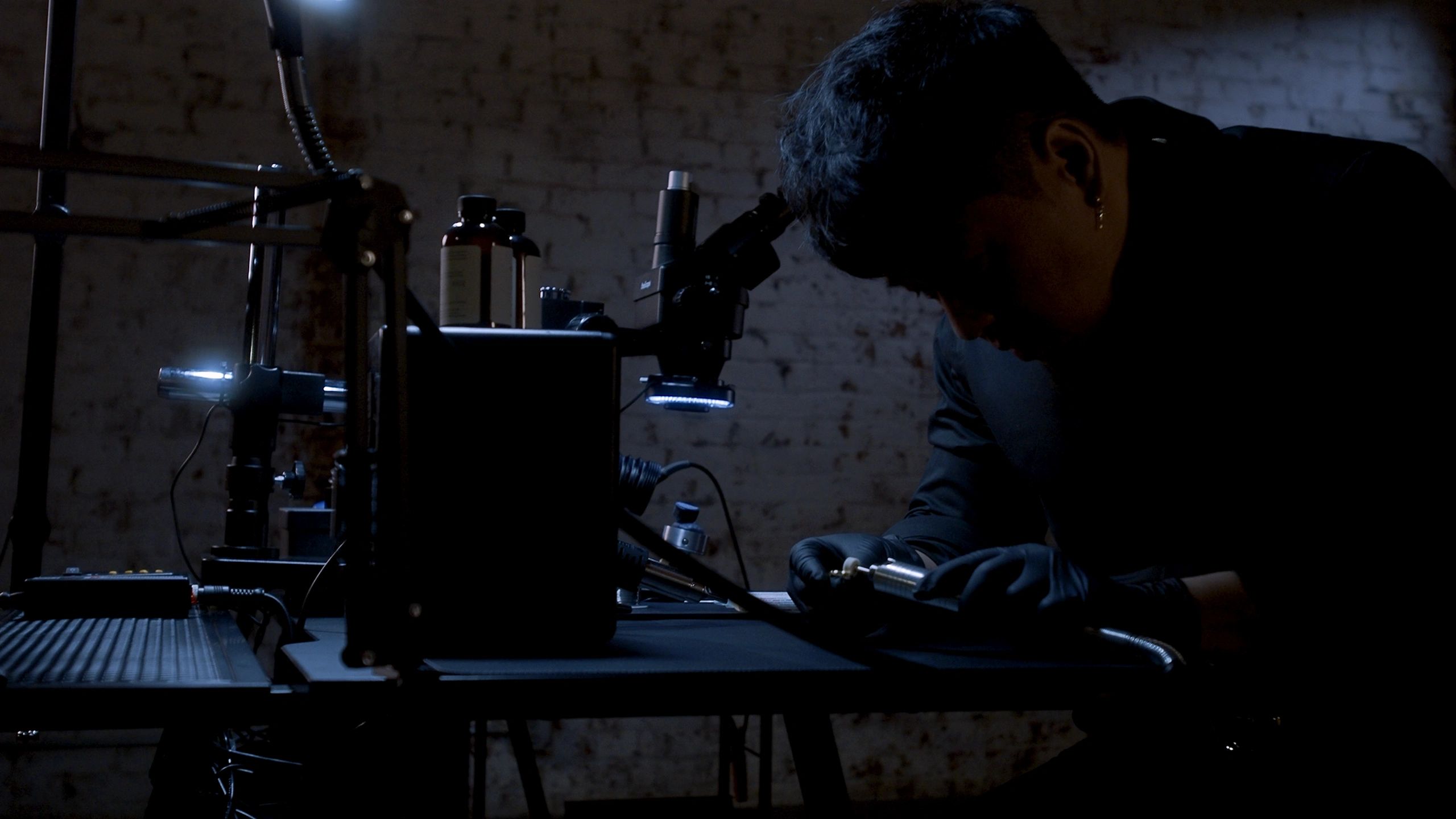 Person examining an object under a microscope in a dimly lit lab.