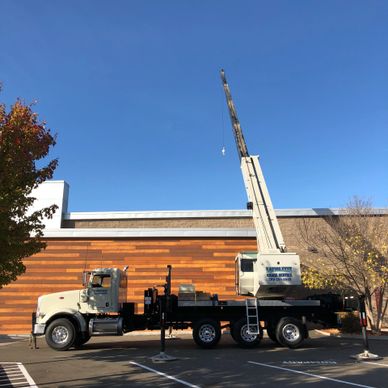 A large crane truck parked with its boom extended against a clear blue sky.
