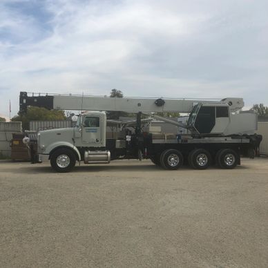 Large white construction crane truck parked on gravel under cloudy sky.