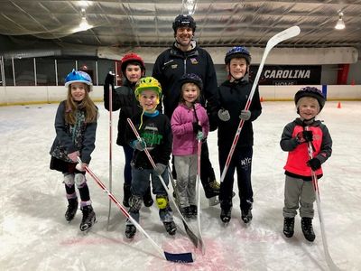 Group of smiling children and an adult on an ice rink with hockey sticks and helmets.