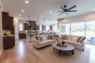 Modern open-concept living room and kitchen with neutral tones and large windows.
