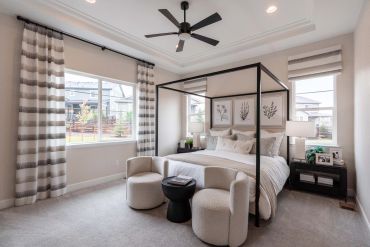 Modern bedroom with a black canopy bed, neutral decor, and cozy seating by the window.