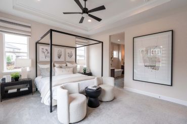 Modern bedroom with a black canopy bed and cozy white chairs.