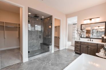 Modern bathroom with glass shower, wooden vanity, and walk-in closet.