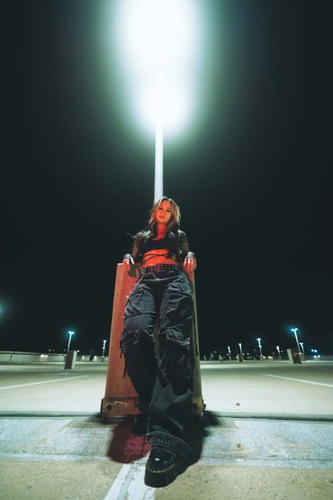 Woman in dark cargo pants and crop top leaning against a light post at night.