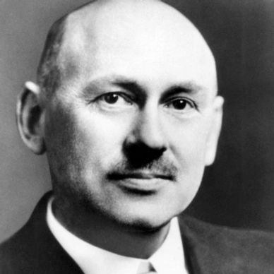 Black and white portrait of a bald man with a mustache in a suit.