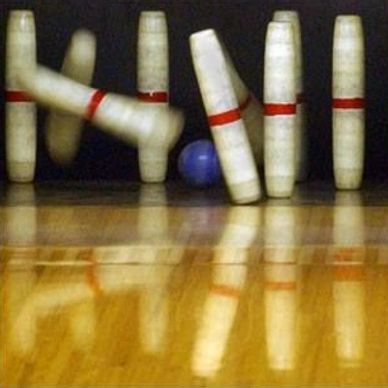 Bowling ball hitting pins, causing them to fall.