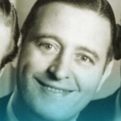 Close-up portrait of a smiling man with slicked-back hair.
