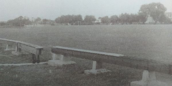 Old wooden benches on a grassy field with trees in the background.