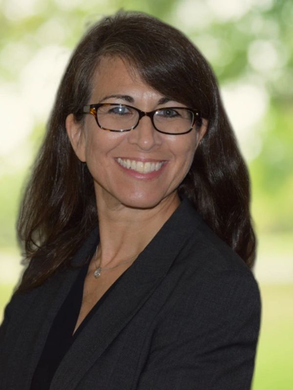 Smiling woman with glasses and dark blazer.