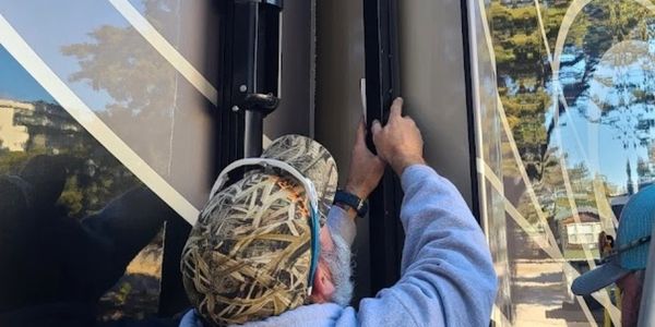 Two men repairing an RV exterior with tools during daytime.