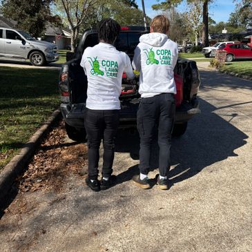 Two people wearing COPA Lawn Care shirts stand by a truck on a sunny street.