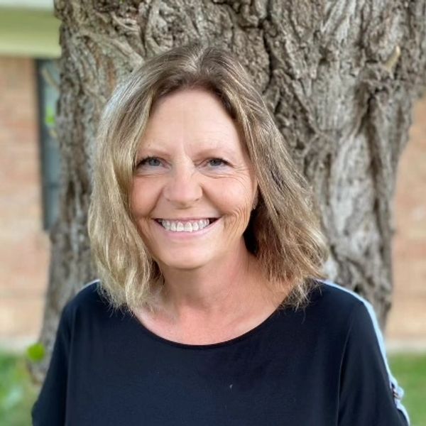 Smiling woman with shoulder-length hair in front of a tree.