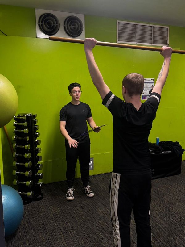 Conducting an overhead squat , to assess muscular imbalances and postural weakness.