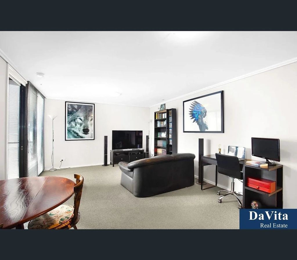 Modern living room with a black leather sofa and artwork on white walls.