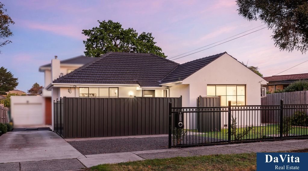 Modern single-story house with black tiled roof and black metal fencing at sunset.