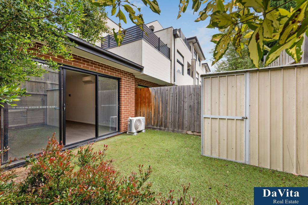 Small backyard with grass, plants, and a shed next to a brick house with sliding glass doors.