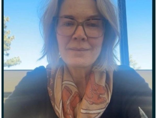 A woman with glasses and a scarf smiling.