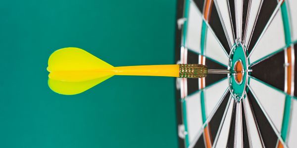 Yellow dart hitting the bullseye on a dartboard.