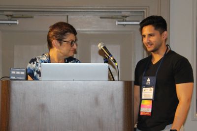 Two people conversing near a podium with a microphone and laptop.