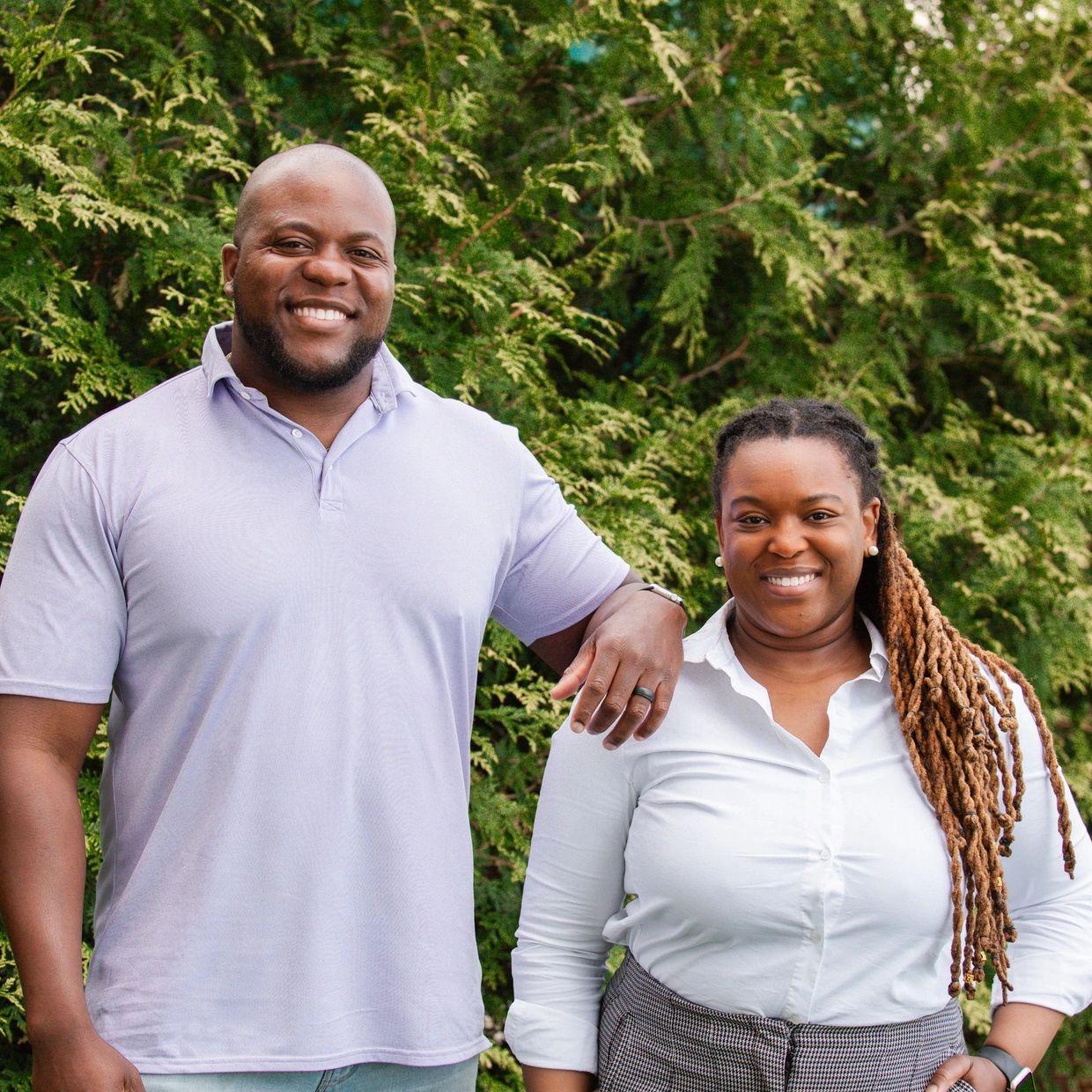 Smiling couple standing outdoors with a green leafy background.