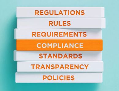 Stack of blocks with compliance-related words, highlighting 'COMPLIANCE' in orange.