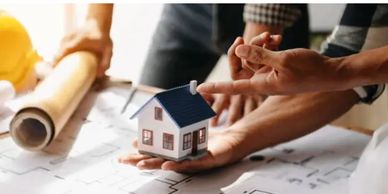 Hands holding a small house model over architectural plans.