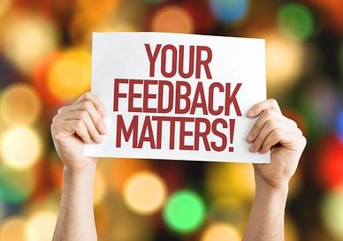 Hands hold a sign that reads 'YOUR FEEDBACK MATTERS!' against a colorful blurred background.