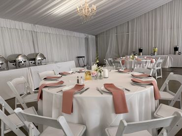 Elegant round table set for an event with white chairs and pink napkins.