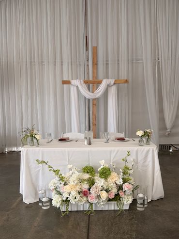 A wedding table with floral arrangement and wooden cross backdrop.