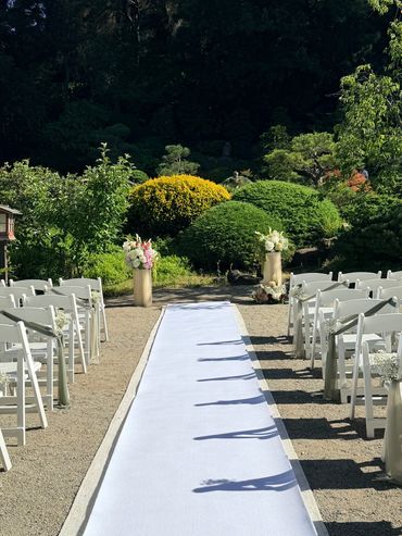 Outdoor wedding aisle with white chairs and floral decorations.