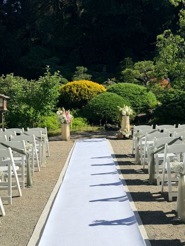 Outdoor wedding aisle with white chairs and floral decorations.