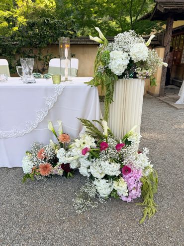 Elegant floral arrangement with white, pink, and orange flowers beside a decorated table outdoors.