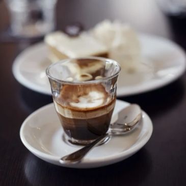 Small glass of espresso on a saucer with a spoon.